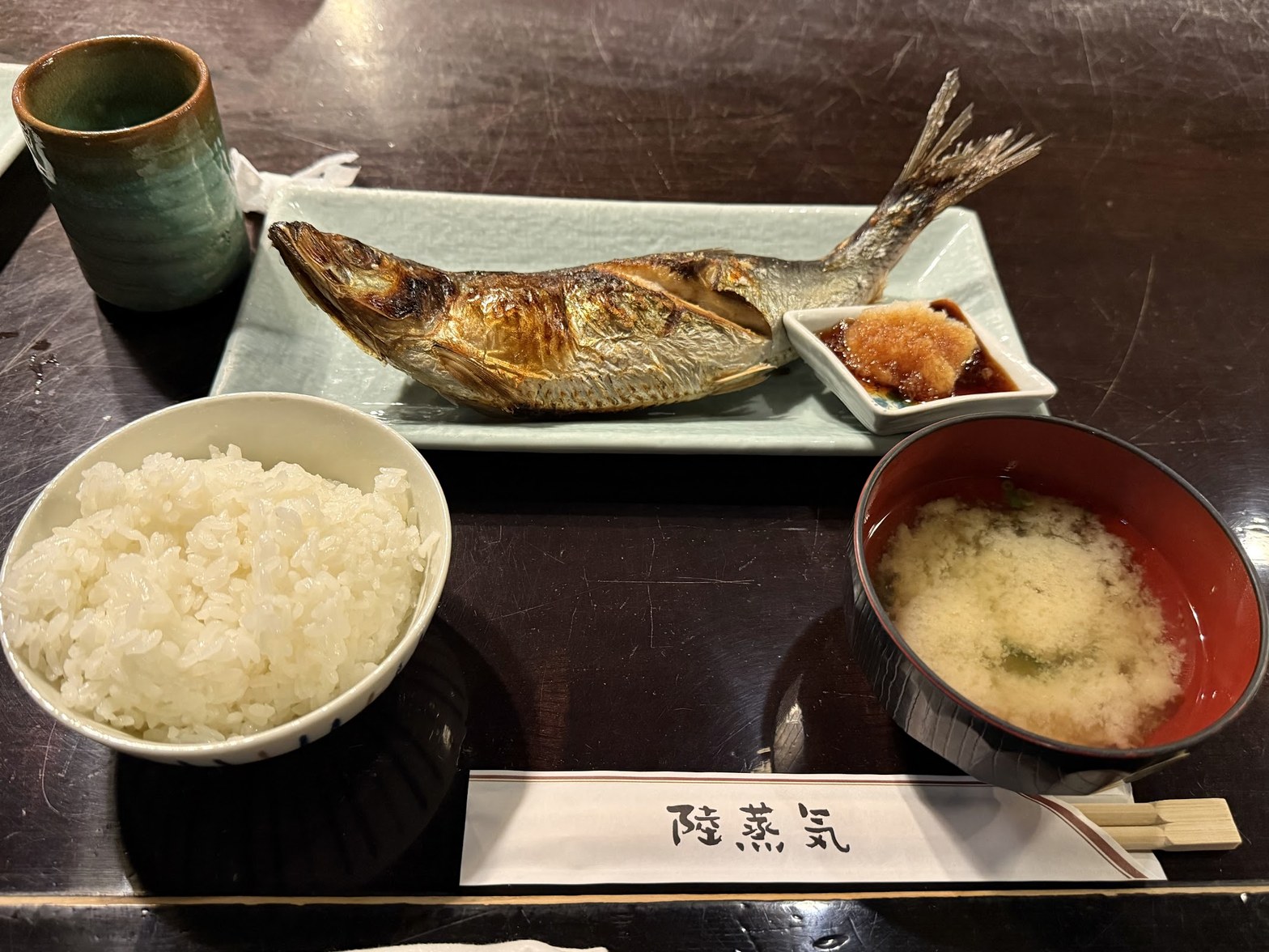 白い茶碗に盛られた白飯、赤い漆椀の味噌汁、青磁の皿に乗った焼き魚、「陸蒸気」と書かれた箸置きカードが並ぶランチ定食